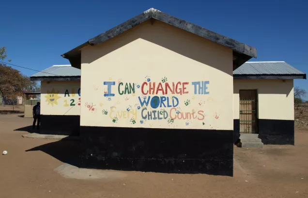 Image of school building against blue sky with colourful handprints and painted letters reading 'I can change the world every child counts'